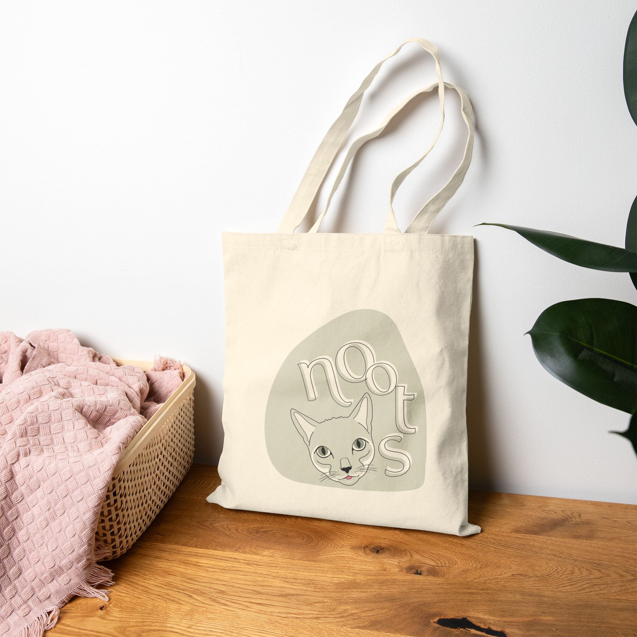 canvas tote bag with a cat design and 'noots' text on a wooden surface with a white wall background.